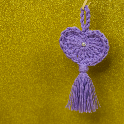 Pingente coração roxo com tassel e pérola sobre fundo amarelo