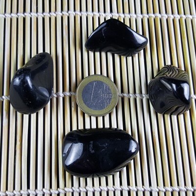 Cinco pedras pretas polidas com uma moeda de 1 euro sobre superfície de bambu