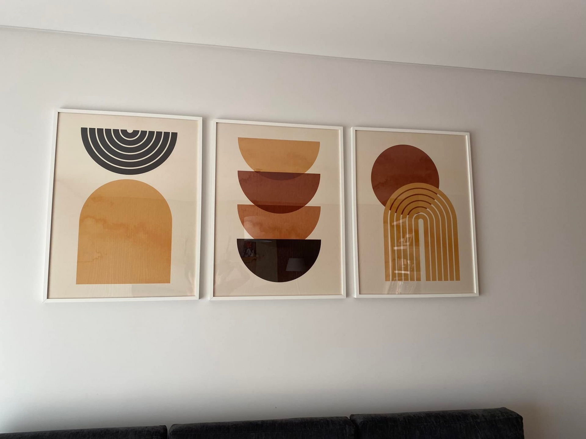 Três quadros abstratos com formas geométricas em tons terrosos na parede, acima de sofá preto
