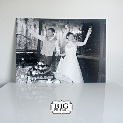 Fotografia preto e branco de casal em celebração com vestido de noiva e colete, sobre mesa branca com etiqueta Big Picture.