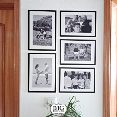 Cinco fotografias a preto e branco com molduras pretas numa parede branca entre portas de madeira e planta verde em vaso.