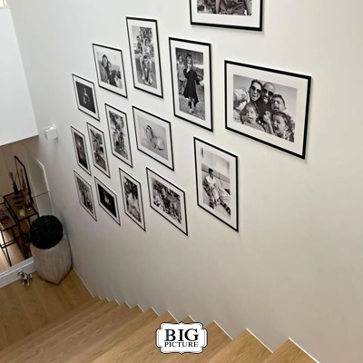 Molduras pretas com fotos em parede branca ao lado de escada de madeira