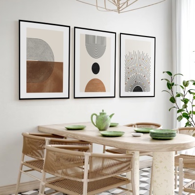 Sala de jantar com mesa oval de madeira clara, cadeiras em corda trançada, louça verde e três quadros geométricos na parede branca.