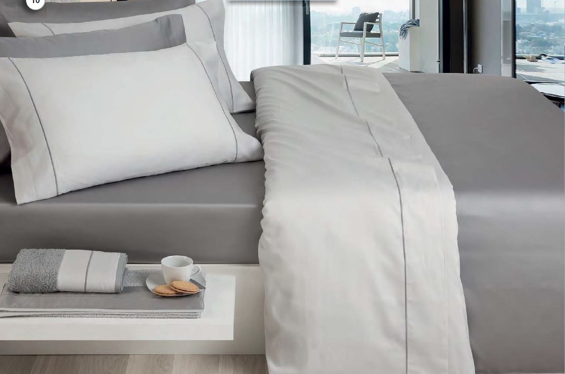 Conjunto de roupa de cama cinza e branco numa cama moderna com janela panorâmica e mesa branca ao lado