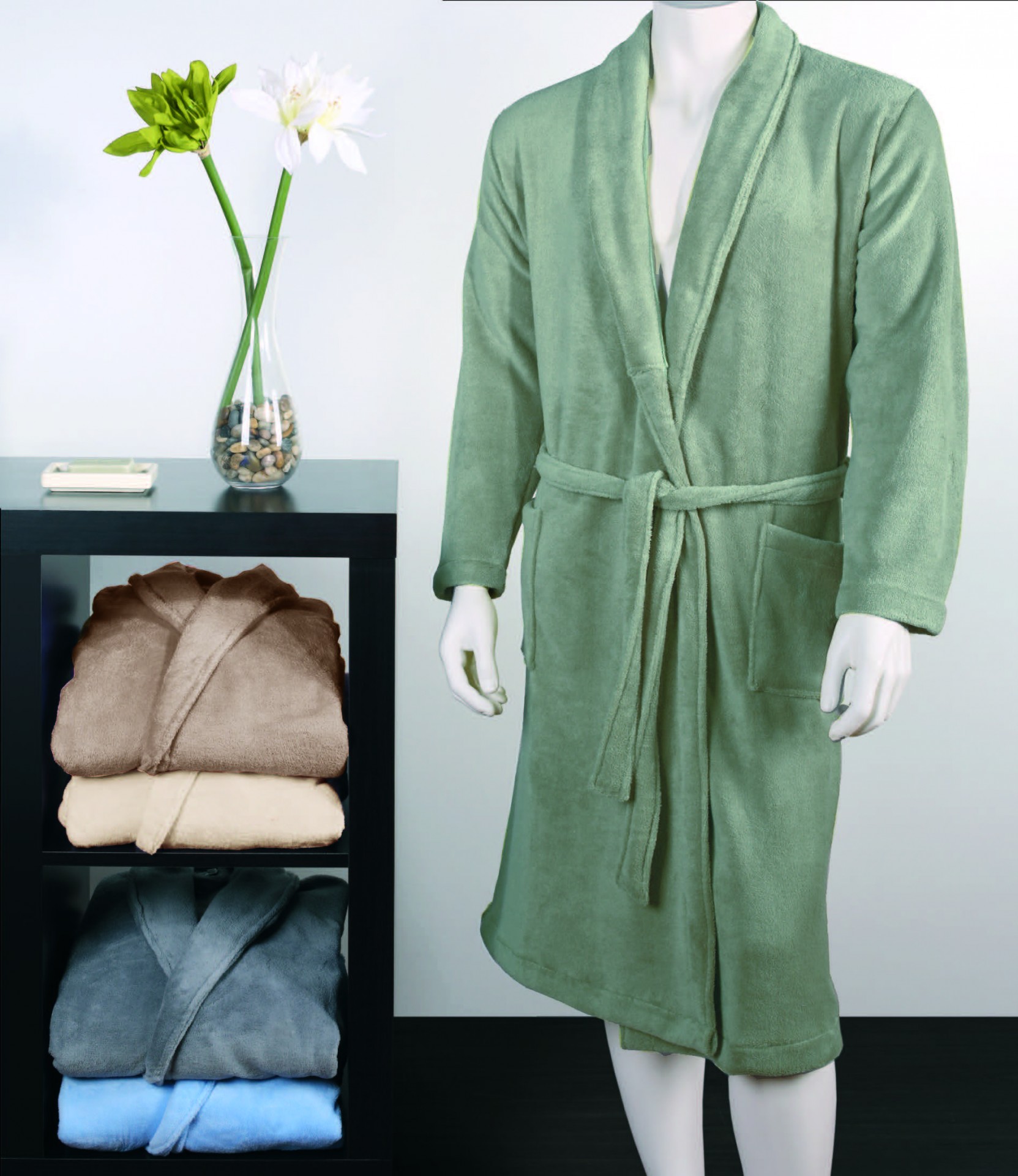 Roupão de banho verde claro em manequim ao lado de estante com roupões dobrados e vaso com flores