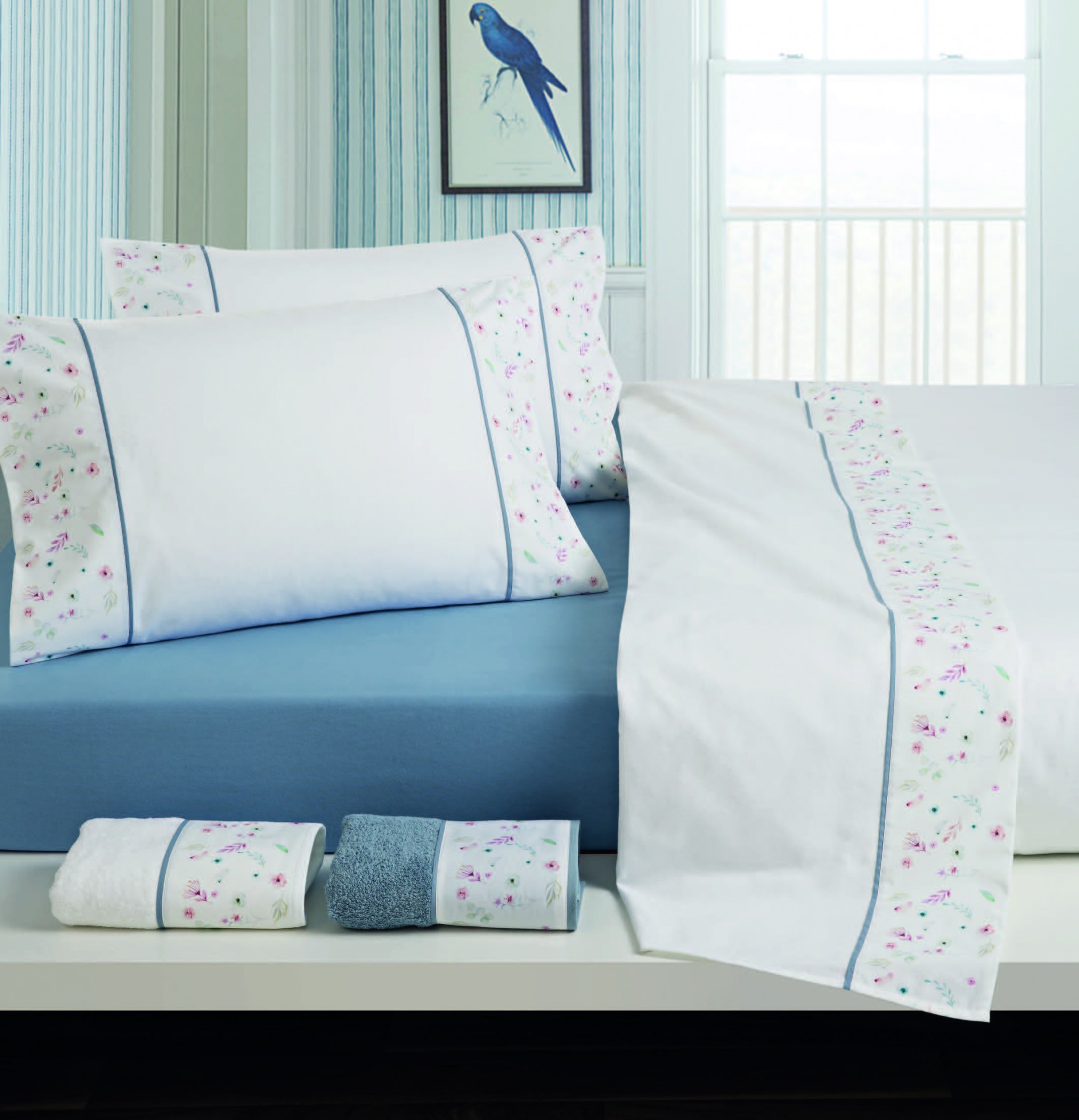 Jogo de cama branco com decoração floral e lençol azul em quarto luminoso