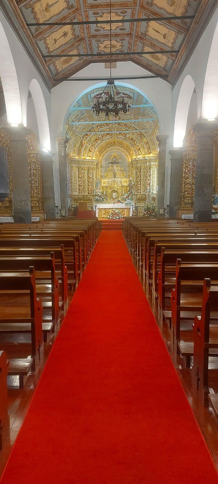 Interior de igreja com bancos de madeira, tapete vermelho e altar dourado