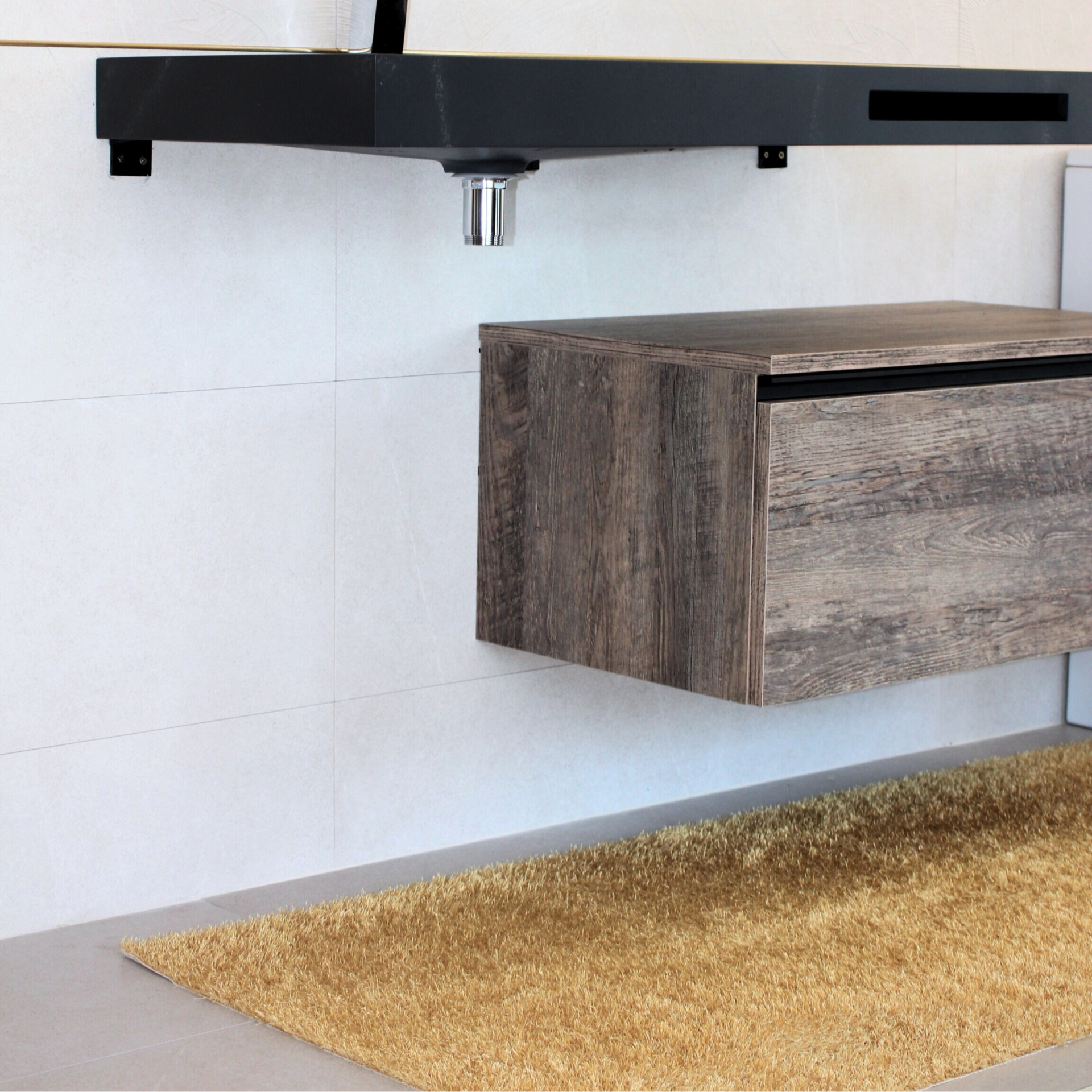 Móvel suspenso em madeira clara com gaveta, loiça preta acima e tapete castanho claro sobre chão cinzento