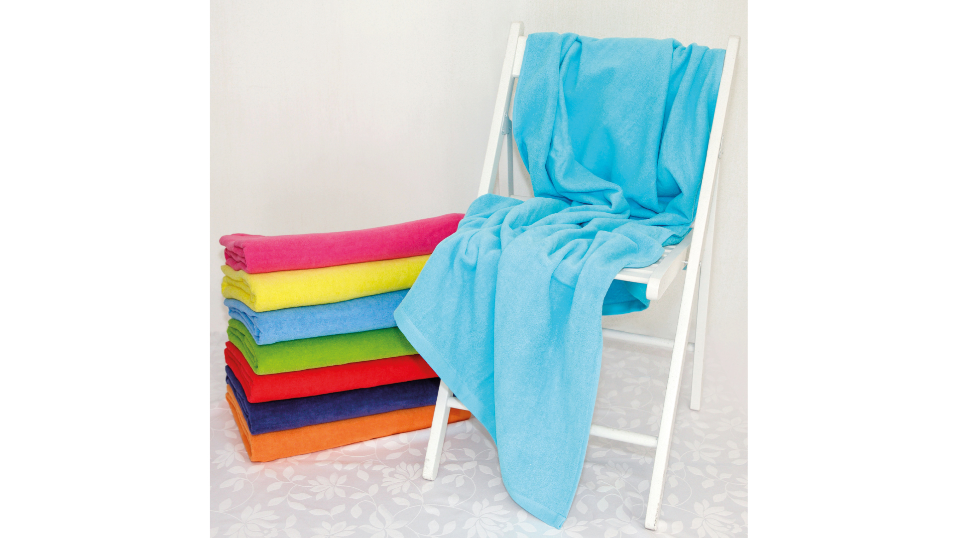 Cadeira branca com toalha azul e pilha de toalhas coloridas dobradas no chão claro