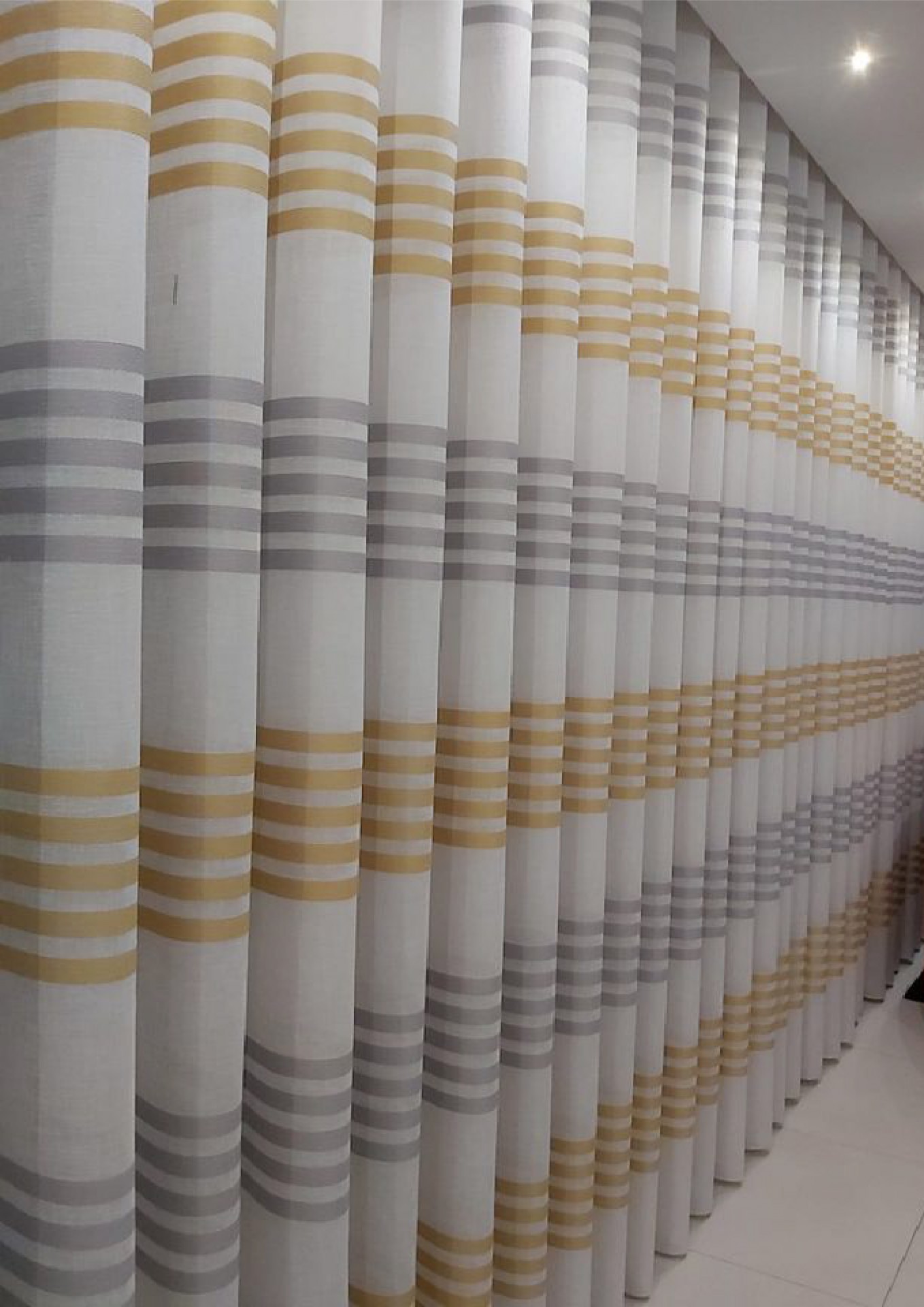 Cortinas brancas com riscas amarelas e cinzentas num ambiente interior