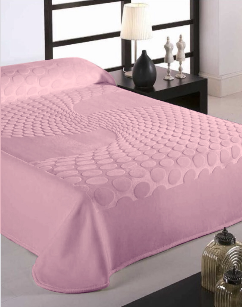 Colcha rosa com padrão de círculos em relevo sobre cama com cabeceira preta e mesa de cabeceira com abajur