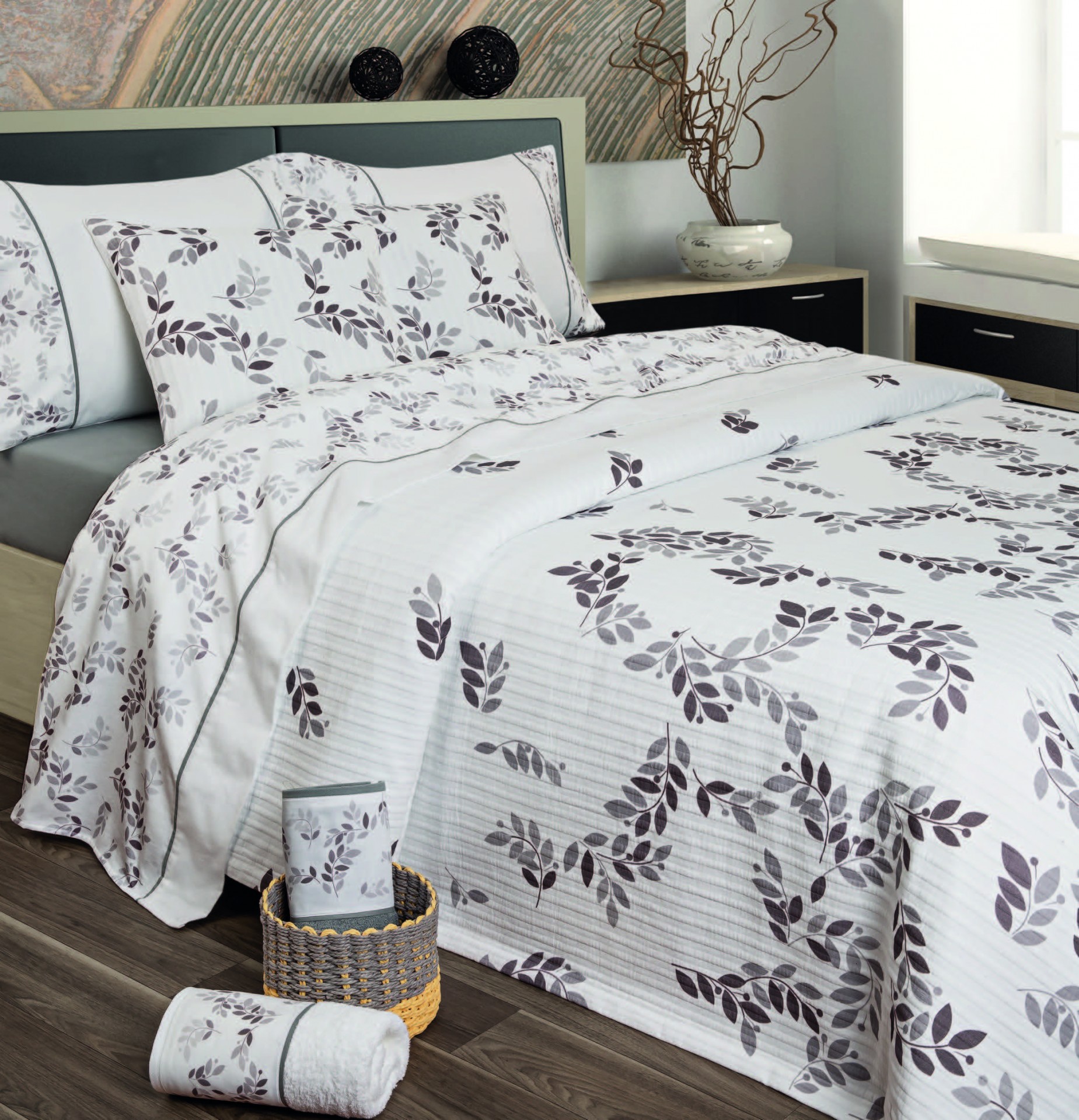 Jogo de cama branco com padrão de folhas cinzentas e pretas numa cama com cabeceira cinza e mesa de cabeceira preta