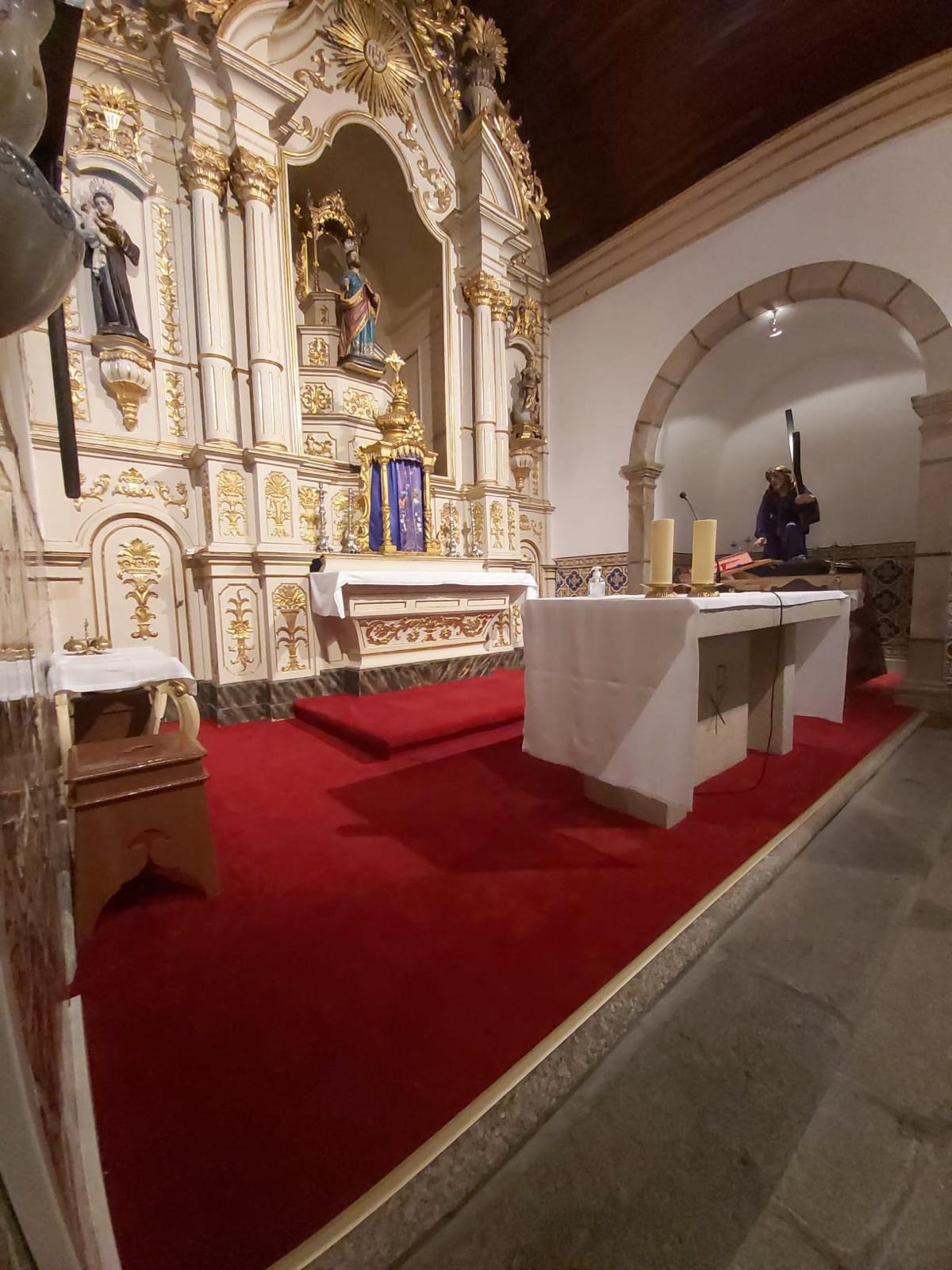 Interior de capela com altar branco e dourado, mesa de altar com toalha branca e carpete vermelho
