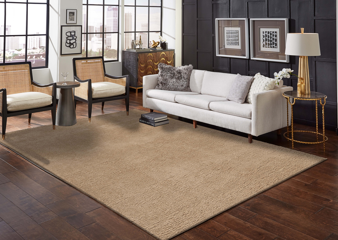 Sala com sofá bege claro, poltronas de madeira e palhinha, tapete bege e mesa dourada