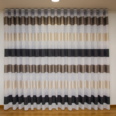 Cortina com padrões horizontais em várias cores pendurada numa parede branca.