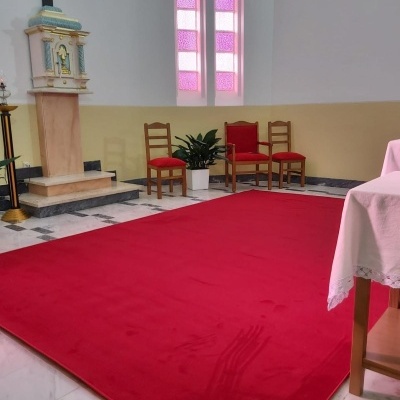 Tapete vermelho grande num chão de mármore com cadeiras de madeira e estrutura religiosa ao fundo