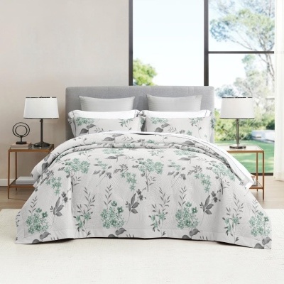 Cama com edredão floral verde e branco numa sala clara com janela grande