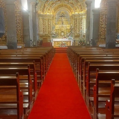 Interior de igreja com bancos de madeira, tapete vermelho e altar dourado