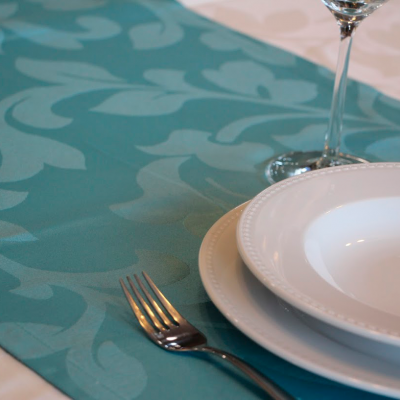 Mesa posta com toalha branca e caminho de mesa azul-claro, pratos brancos, garfo e copo