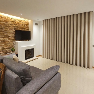 Sala de estar com sofá cinza, cortinas bege e parede decorativa de pedra