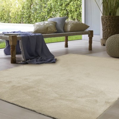 Almofadão bege retangular numa sala clara ao lado de banco de madeira e pufe de crochê