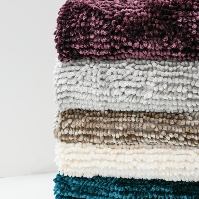 Pilhas de tapetes chenille em quatro cores variadas sobre superfície branca