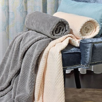 Mantas texturizadas cinza e creme sobre cadeira azul com almofada, ao lado de mesa com revista.
