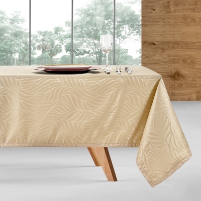 Toalha de mesa bege com padrão de folhas em tecido jacquard sobre mesa de madeira clara.