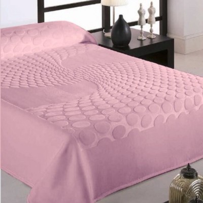 Colcha rosa com padrão de círculos em relevo sobre cama com cabeceira preta e mesa de cabeceira com abajur