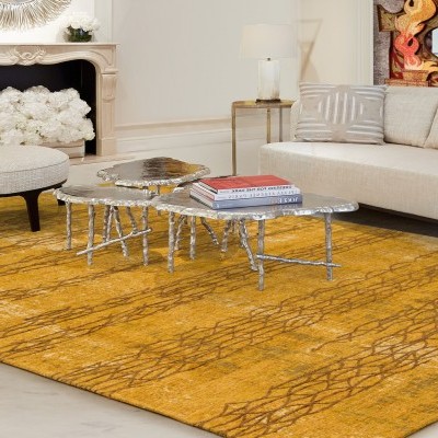 Tapete amarelo com padrão castanho numa sala com sofá bege e mesa de centro prateada