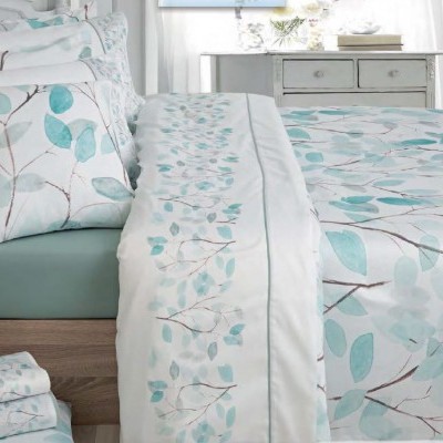 roupa de cama com padrão de folhas azul e verde e almofada decorativa num quarto com móvel cinzento