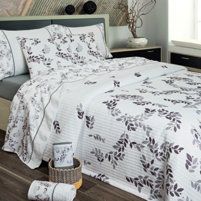 Jogo de cama branco com padrão de folhas cinzentas e pretas numa cama com cabeceira cinza e mesa de cabeceira preta