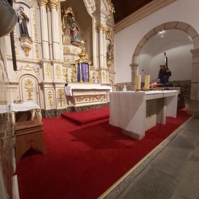 Interior de capela com altar branco e dourado, mesa de altar com toalha branca e carpete vermelho