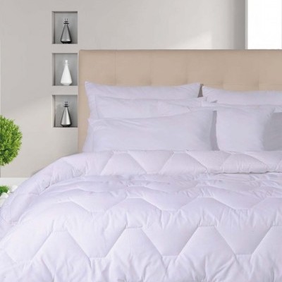 Cama com edredão branco acolchoado hexagonal e almofadas brancas numa cabeceira bege