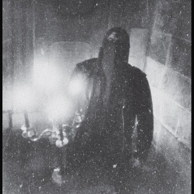 Pessoa com capuz em ambiente interior escuro e paredes de pedra com candelabro aceso