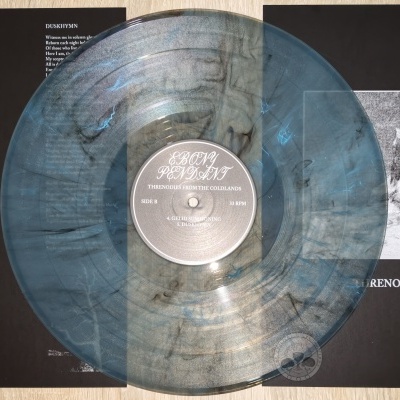 Disco de vinil cinzento translúcido com capa preta aberta mostrando texto e imagem de montanhas