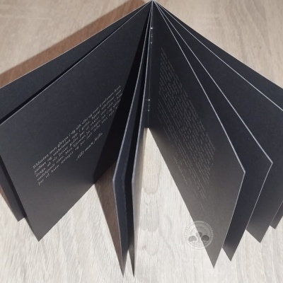 Livro ou brochura com páginas pretas e texto branco, sobre madeira clara