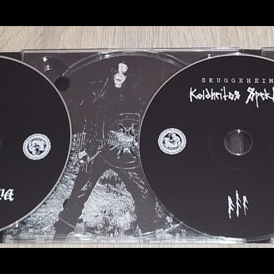 Caixa aberta de CD com três discos pretos e capas com texto branco sobre fundo escuro