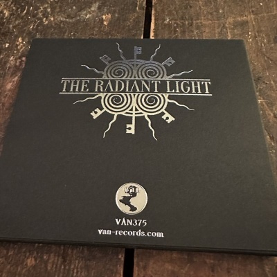 Capa de disco THE RADIANT LIGHT com símbolo e texto sobre fundo preto e cinza