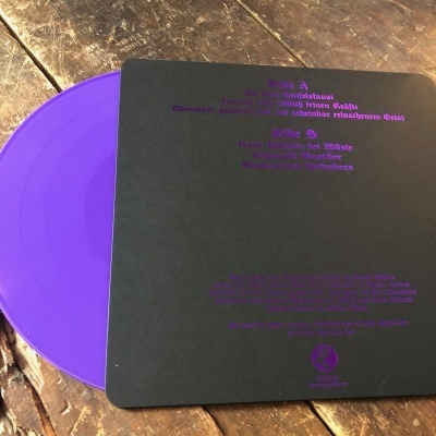 Disco vinil roxo com capa preta e texto roxo sobre superfície de madeira