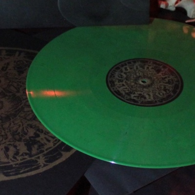 Disco de vinil verde com padrão central preto sobre capa com design circular