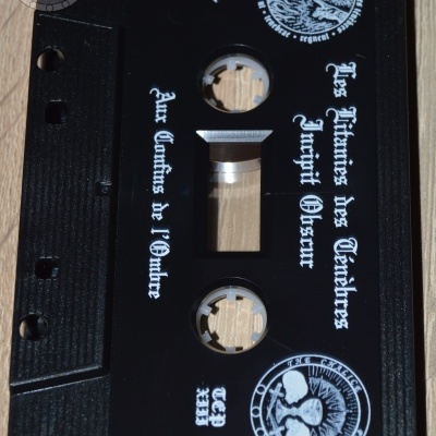 Cassete de áudio preta com texto branco em estilo gótico e imagens circulares com caveiras.