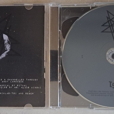 CD musical cinzento com símbolo preto, em estojo transparente aberto, contracapa com figura e texto pequeno