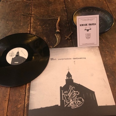 Disco de vinil preto com capa de igreja estilizada, livrinho rosa SHALE SHOES, lâmina curva e cruz de madeira sobre mesa de madeira.