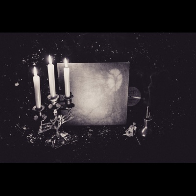 Candelabro metálico com velas acesas, objeto quadrado ao fundo, vaso e ornamento em superfície escura