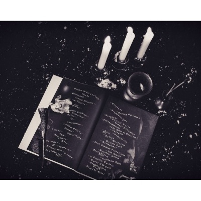 Livro aberto com texto, velas acesas, copo e ramos sobre mesa escura