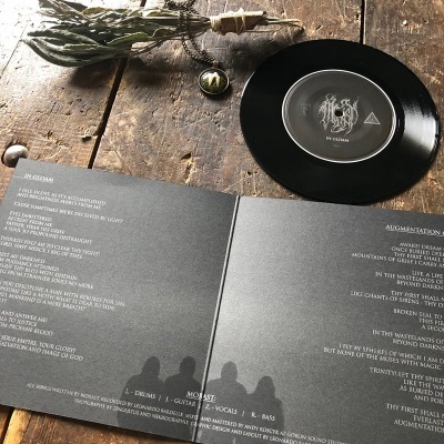 Disco vinil preto com capa dupla aberta com letras, ramo seco e selo de metal sobre mesa de madeira