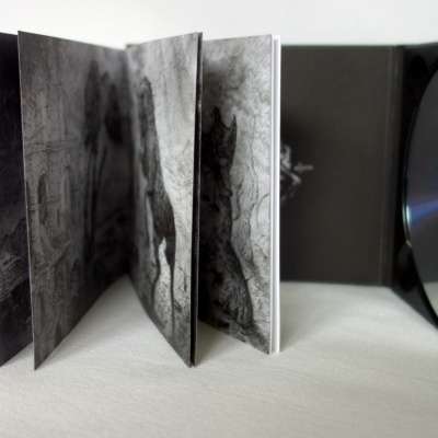 Caixa de CD preta aberta com disco prateado e folheto visível