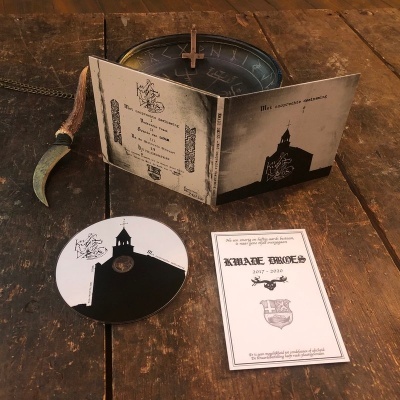 CD Kreape Bones 2017-2020 em capa com imagem de igreja, junto com panfleto e foice pequena sobre mesa de madeira.