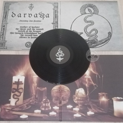Disco de vinil preto sobre capa com ilustração de velas e caveira e texto DARVAÇA em papel ao lado